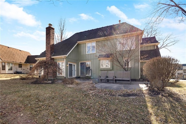 back of house featuring a patio, a yard, a chimney, and board and batten siding