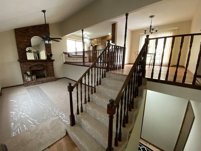 staircase with ceiling fan with notable chandelier and a fireplace