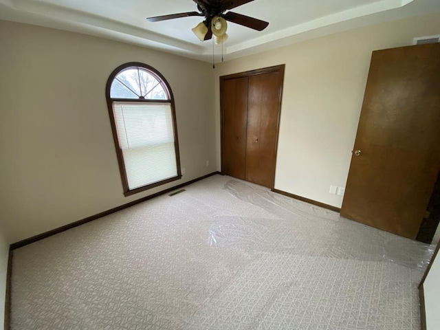 unfurnished bedroom featuring ceiling fan, a closet, light carpet, and a raised ceiling