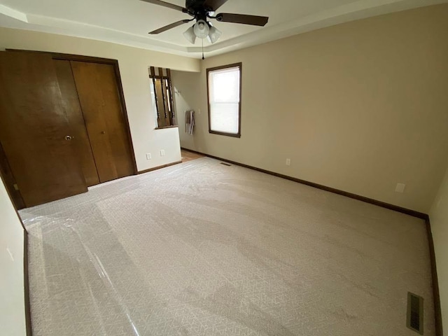 unfurnished bedroom featuring ceiling fan, light colored carpet, a closet, and a tray ceiling