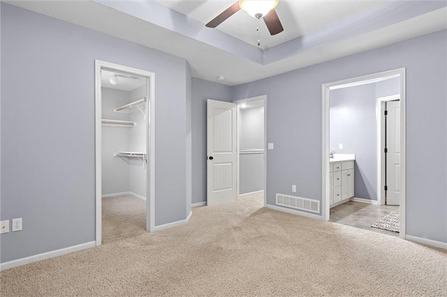 unfurnished bedroom featuring connected bathroom, ceiling fan, light colored carpet, and a spacious closet