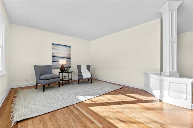 living area featuring baseboards, wood finished floors, and ornate columns