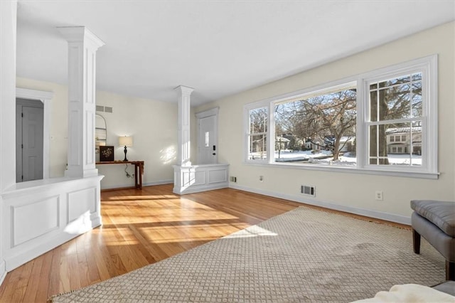 living area with ornate columns, baseboards, visible vents, and wood finished floors