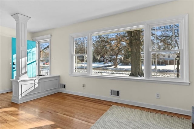 interior space with light wood-type flooring, visible vents, decorative columns, and baseboards