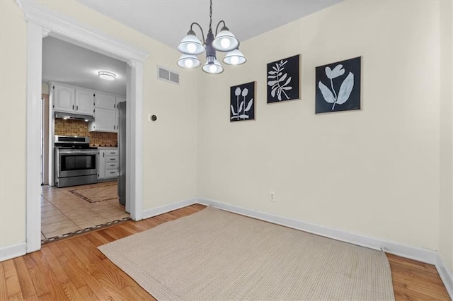 unfurnished dining area with baseboards, a chandelier, visible vents, and light wood-style floors