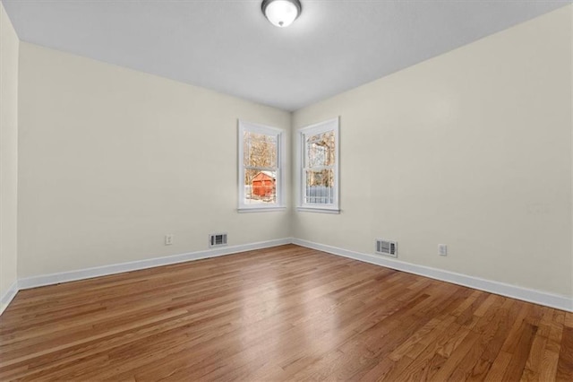 spare room with baseboards, visible vents, and wood finished floors