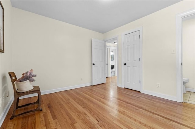 bedroom with ensuite bath, light wood-style flooring, and baseboards