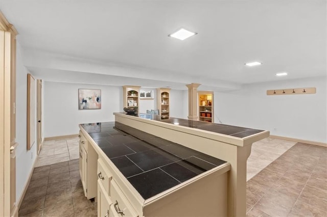 kitchen featuring baseboards, tile counters, open floor plan, cream cabinetry, and ornate columns