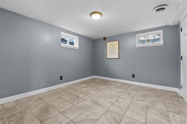 basement featuring baseboards, a textured ceiling, visible vents, and a wealth of natural light