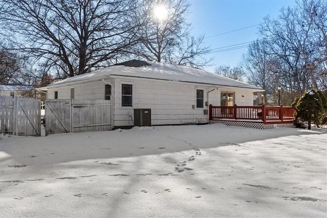 snow covered house with a deck, central AC unit, and fence