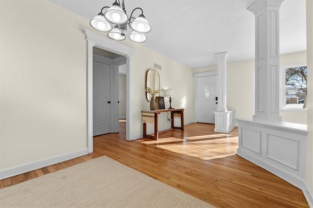 interior space featuring a notable chandelier, visible vents, baseboards, light wood-style floors, and ornate columns