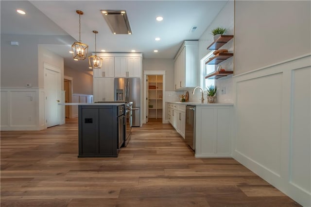 kitchen featuring appliances with stainless steel finishes, white cabinetry, a center island, decorative backsplash, and decorative light fixtures