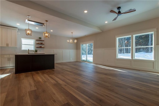 kitchen with hanging light fixtures, dark hardwood / wood-style floors, tasteful backsplash, a kitchen island, and ceiling fan with notable chandelier