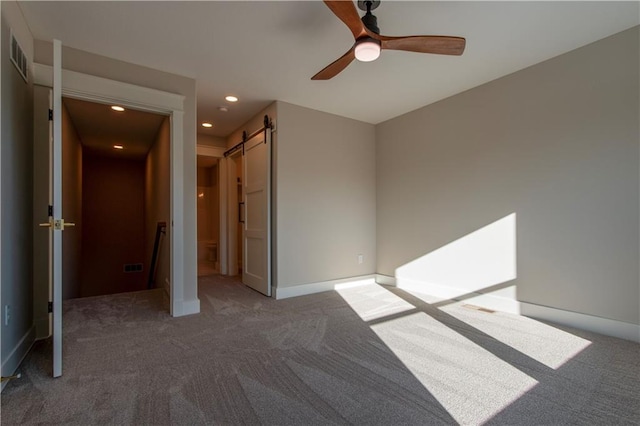 unfurnished bedroom featuring ceiling fan, a barn door, and dark colored carpet