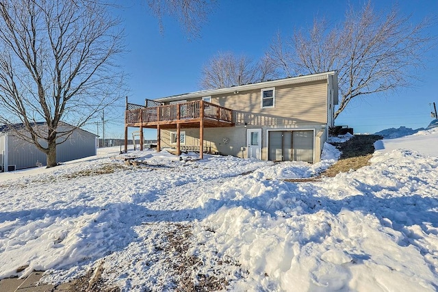 snow covered back of property featuring a garage and a wooden deck