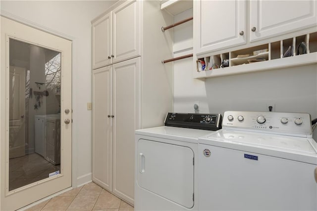 clothes washing area with light tile patterned floors, washing machine and dryer, and cabinets