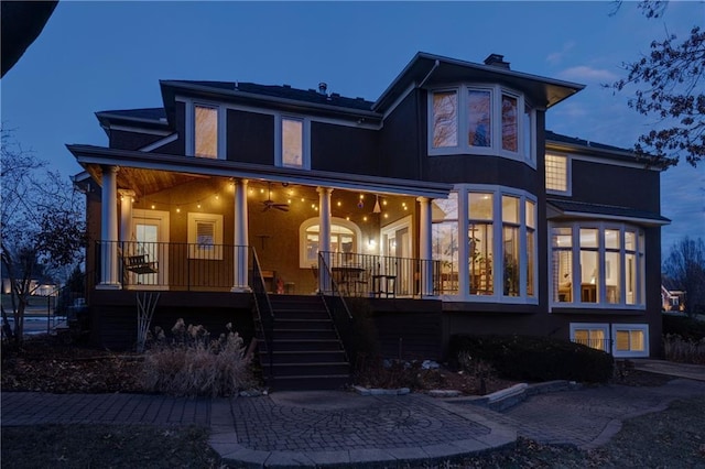 back of property with covered porch, a chimney, and stairs