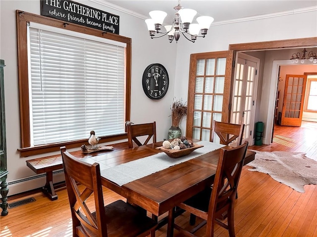 dining area with crown molding, french doors, light hardwood / wood-style flooring, and a notable chandelier