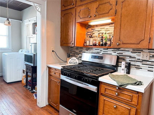 kitchen with decorative backsplash, stainless steel appliances, hardwood / wood-style flooring, washer / clothes dryer, and hanging light fixtures