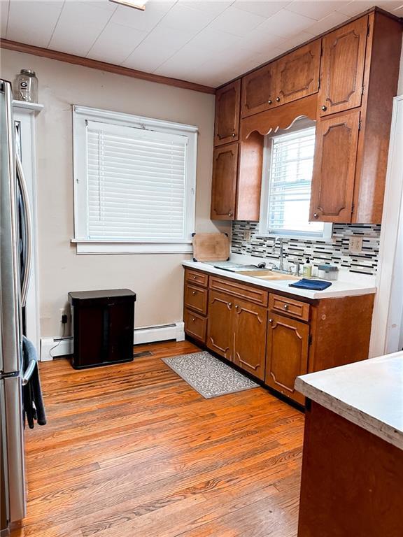 kitchen with light hardwood / wood-style flooring, baseboard heating, ornamental molding, and sink