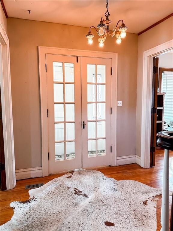 entryway with french doors, light hardwood / wood-style flooring, and an inviting chandelier