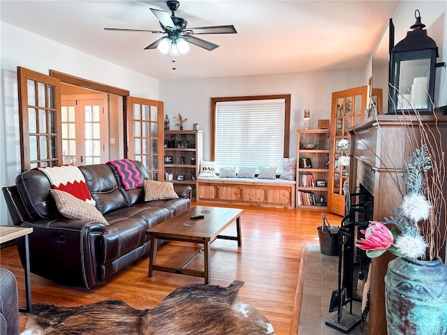 living room with a brick fireplace, ceiling fan, french doors, and light hardwood / wood-style flooring