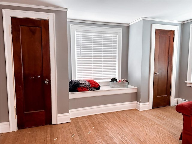 corridor with baseboard heating, crown molding, and light hardwood / wood-style flooring