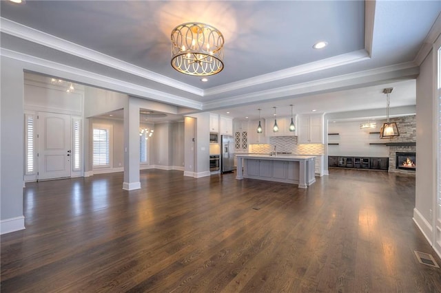 unfurnished living room featuring a raised ceiling, a stone fireplace, a chandelier, and dark hardwood / wood-style floors