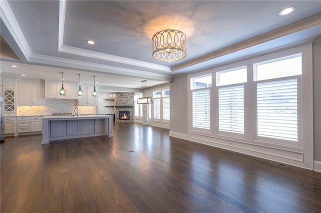 unfurnished living room featuring ornamental molding, a tray ceiling, an inviting chandelier, dark hardwood / wood-style floors, and a stone fireplace