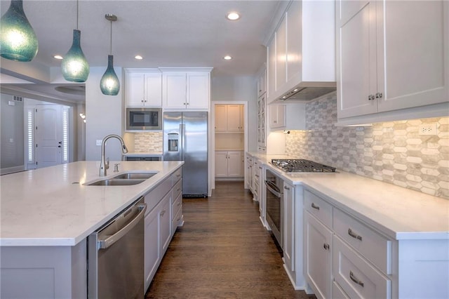 kitchen with sink, built in appliances, wall chimney exhaust hood, decorative light fixtures, and white cabinetry