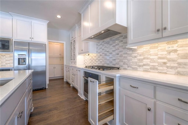 kitchen featuring built in appliances, wall chimney exhaust hood, decorative backsplash, dark hardwood / wood-style flooring, and white cabinetry