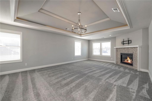 unfurnished living room with a tray ceiling, a tile fireplace, carpet flooring, and an inviting chandelier