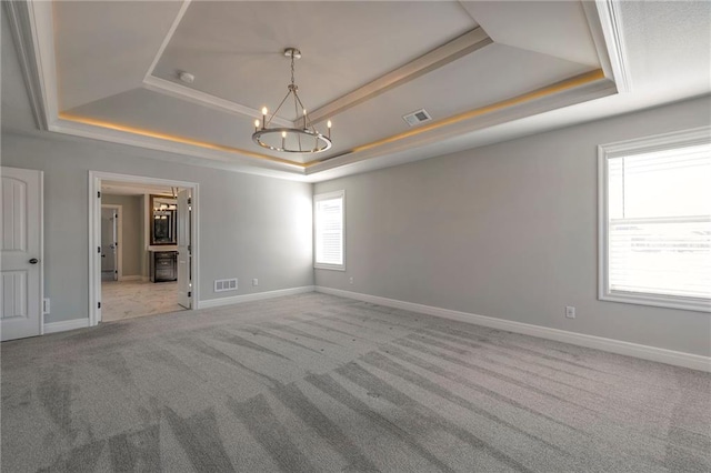 carpeted spare room featuring a tray ceiling and an inviting chandelier