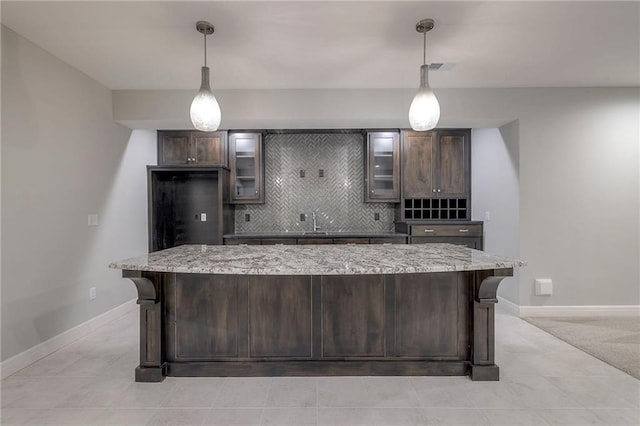 kitchen with dark brown cabinetry, light stone countertops, a center island, and hanging light fixtures