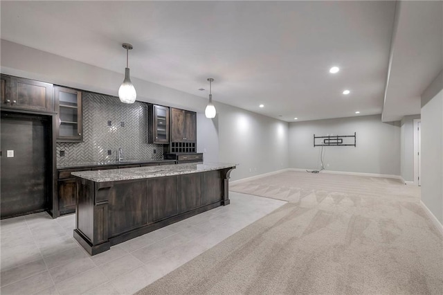 kitchen featuring dark brown cabinetry, light stone counters, a center island, and pendant lighting