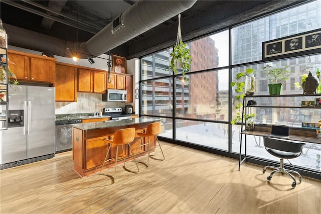 kitchen featuring a center island, stainless steel appliances, dark stone counters, a breakfast bar, and light wood-type flooring