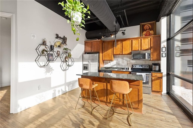 kitchen with backsplash, dark stone counters, stainless steel appliances, light hardwood / wood-style floors, and a kitchen island