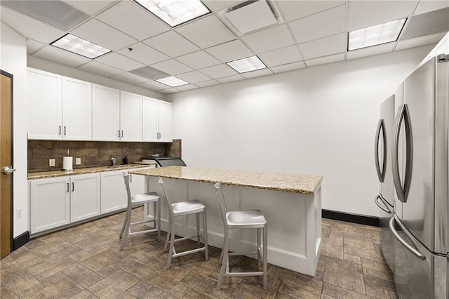 kitchen featuring stainless steel fridge, light stone counters, and white cabinetry