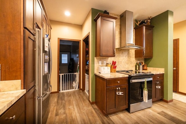 kitchen with wall chimney exhaust hood, stainless steel appliances, light stone counters, backsplash, and light hardwood / wood-style floors