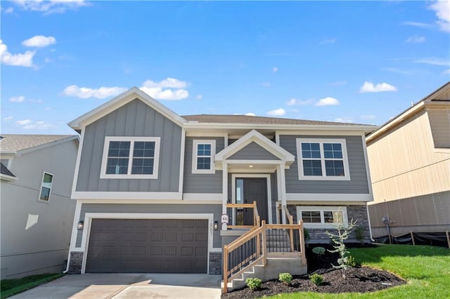 split foyer home featuring stone siding, board and batten siding, an attached garage, and driveway