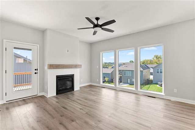 unfurnished living room with wood finished floors, baseboards, visible vents, a ceiling fan, and a glass covered fireplace