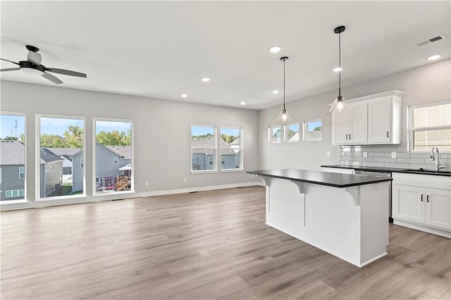 kitchen featuring visible vents, a sink, light wood-style floors, dark countertops, and tasteful backsplash