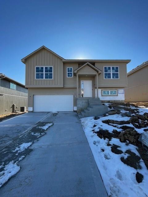 bi-level home with board and batten siding, driveway, a garage, and fence