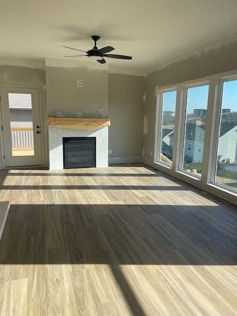 unfurnished living room featuring a wealth of natural light, a glass covered fireplace, crown molding, and wood finished floors