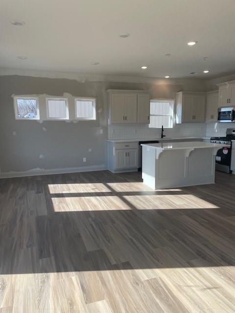 kitchen featuring backsplash, a kitchen island, baseboards, appliances with stainless steel finishes, and white cabinetry