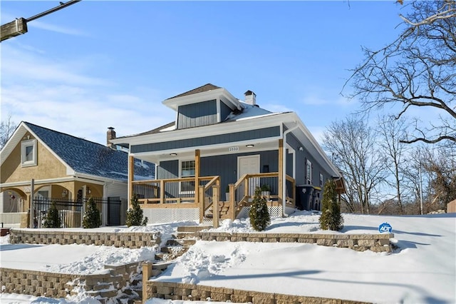 snow covered rear of property featuring covered porch