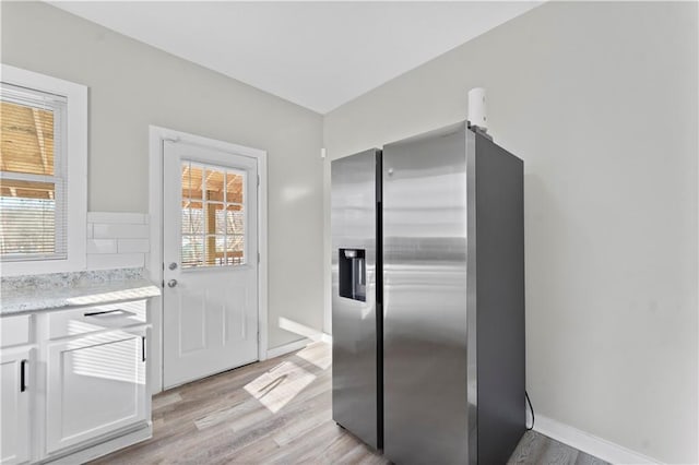 kitchen with white cabinets, stainless steel refrigerator with ice dispenser, light hardwood / wood-style floors, and light stone counters