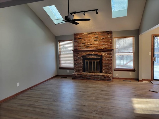 unfurnished living room featuring wood-type flooring, a skylight, a brick fireplace, and ceiling fan