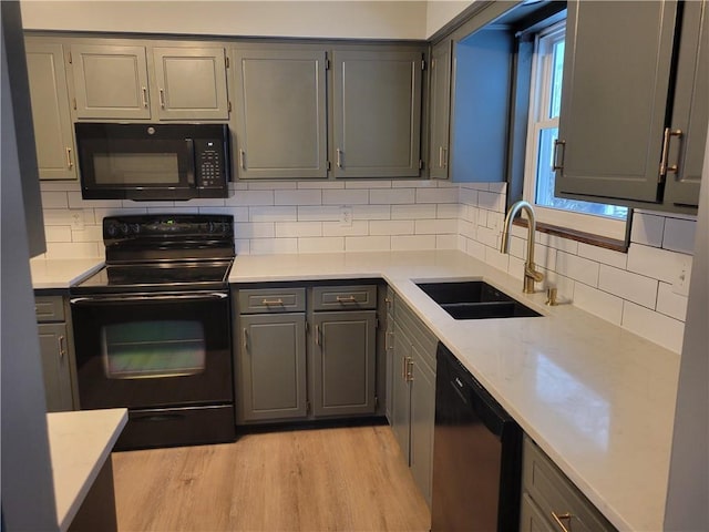 kitchen with sink, light hardwood / wood-style floors, gray cabinets, decorative backsplash, and black appliances