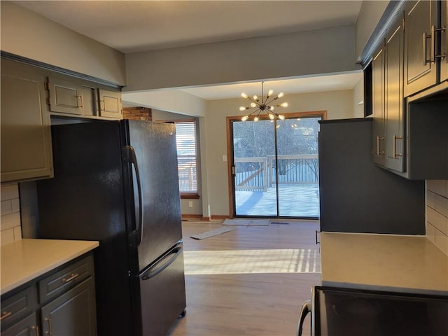 kitchen with hanging light fixtures, black fridge, a chandelier, light hardwood / wood-style floors, and decorative backsplash